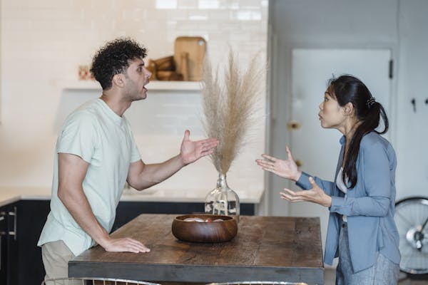 A couple engages in a heated argument at a wooden table in a modern indoor setting.