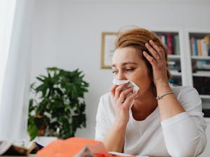 An adult woman feeling unwell, blowing her nose indoors.