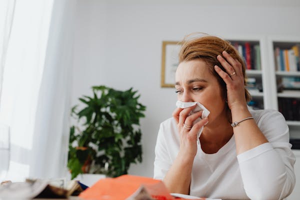 An adult woman feeling unwell, blowing her nose indoors.