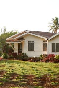 A beautiful house in Valencia City, Philippines, surrounded by a vibrant garden under a clear sky. lush tropical landscaping around a home, featuring large trees providing shade for the facade.