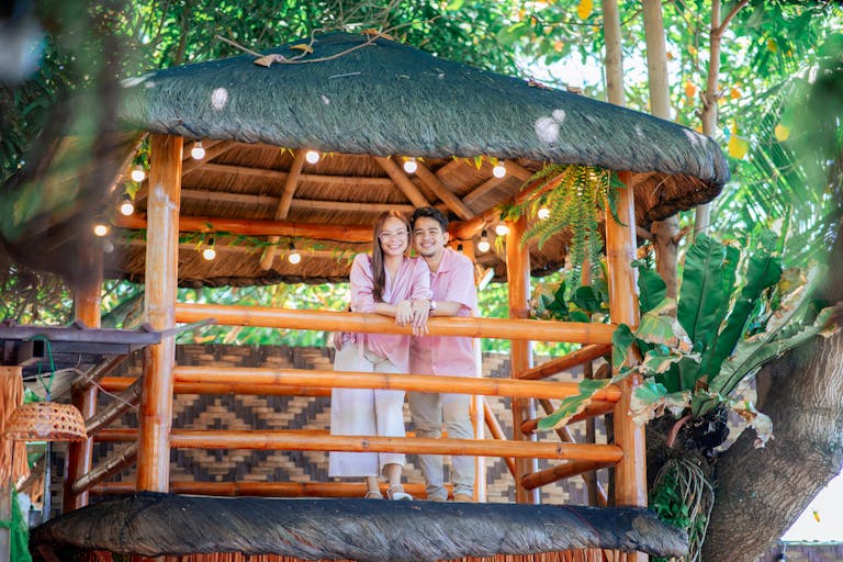 A happy couple enjoying a cozy moment on a wooden treehouse surrounded by lush greenery.