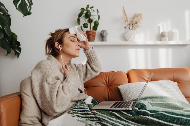 Woman sitting on couch with a laptop and earphones, looking relaxed indoors.